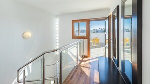 Ein modernes Interieur mit einer Holztreppe, einem Glasgeländer und Blick auf die Terrasse mit gelben Stühlen.