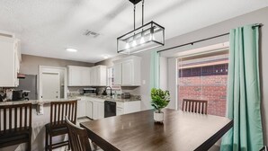 A modern kitchen with white cabinets, a dining table with chairs, and a potted plant. - 4BDR+GameRoom+GroupsWelcome+Extd Stay Discounts (Corpus Christi)