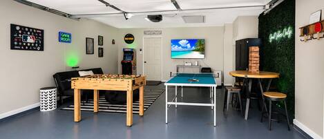 Una stanza con un tavolo da calcio, un biliardo, una televisione e un neon.