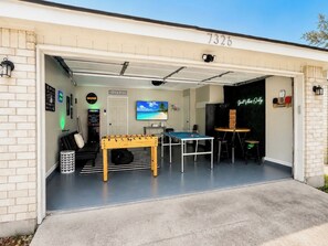 Un garage équipé d’une table de baby-foot, d’une table de billard et d’un téléviseur fixé au mur.