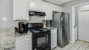 A kitchen with white cabinets, a black stove, a stainless steel refrigerator, and a Keurig coffee maker. - 4BDR+GameRoom+GroupsWelcome+Extd Stay Discounts (Corpus Christi)