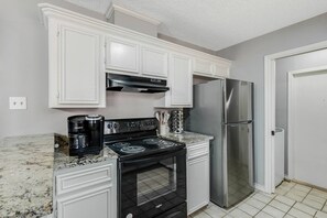 A kitchen with white cabinets, a black stove, a stainless steel refrigerator, and a Keurig coffee maker.