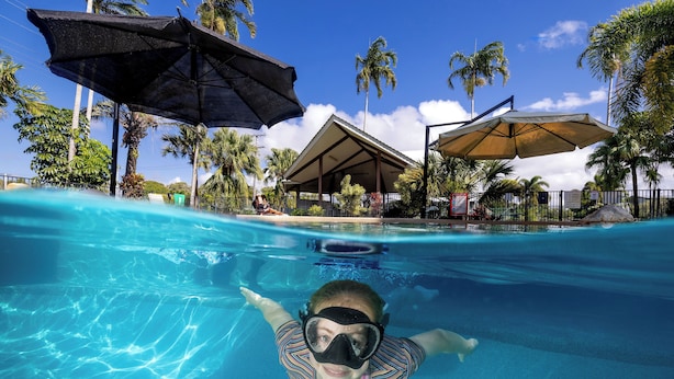 A swimming pool with clear blue water, surrounded by palm trees and umbrellas.