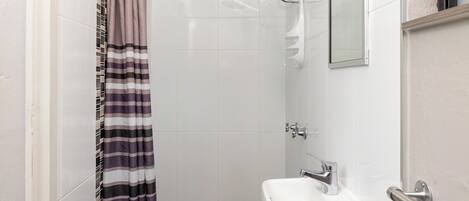 Une petite salle de bain propre, équipée d’une douche, d’un lavabo et d’un miroir.