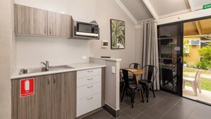 A kitchenette with a microwave, sink, and cabinets. There is a fire extinguisher sign on the cabinet. A table and chairs are visible in the adjacent area.