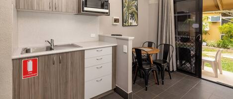 A kitchenette with a microwave, sink, and cabinets. There is a fire extinguisher sign on the cabinet. A table and chairs are visible in the adjacent area.