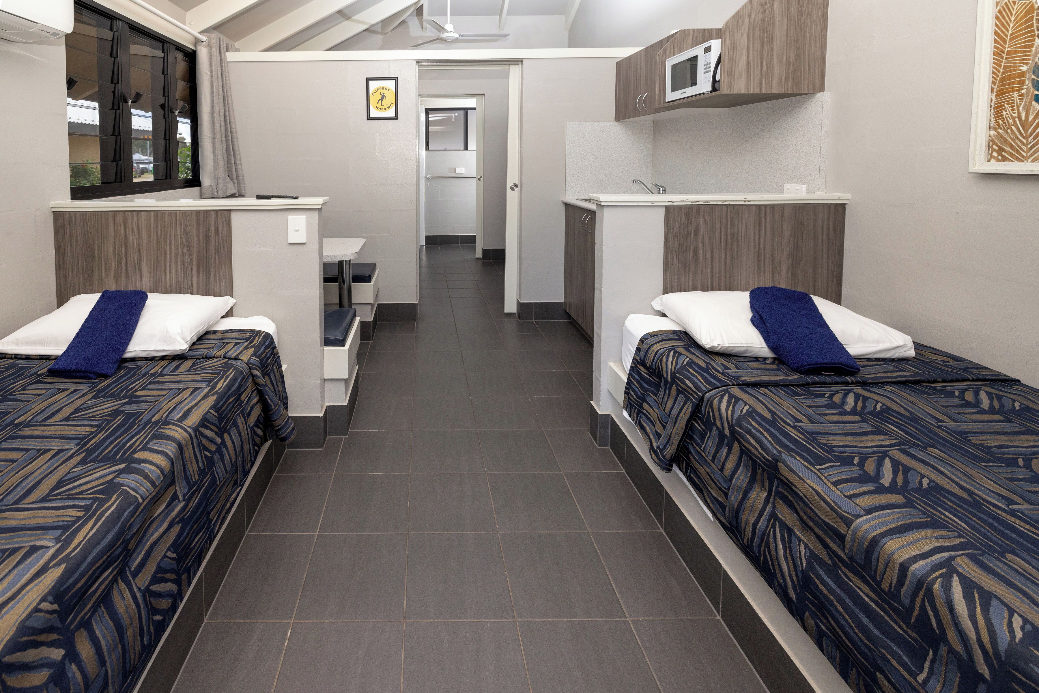 A hotel room with two beds, a kitchenette, a bathroom, and a small sitting area.