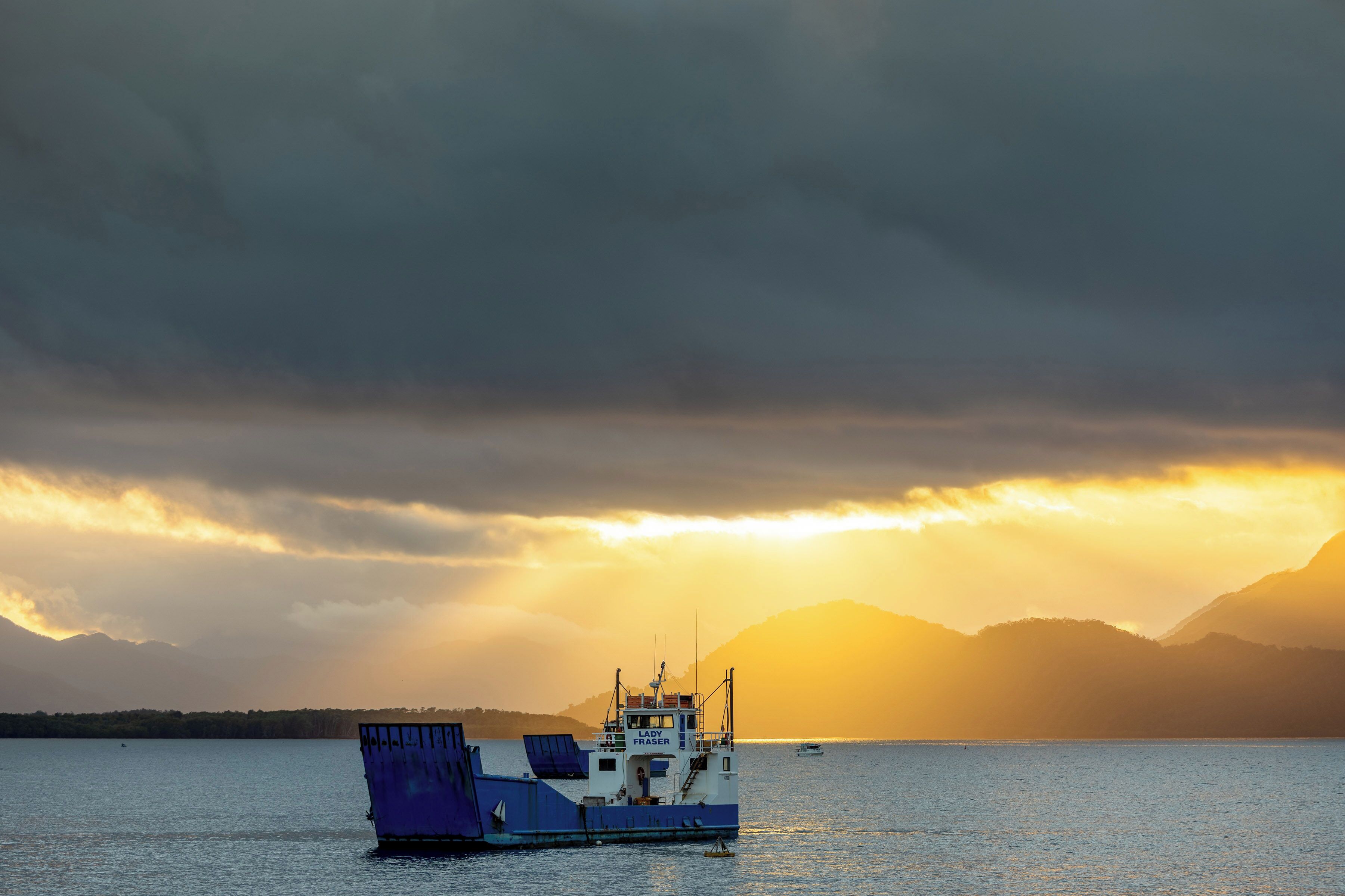 A ferry boat named LADY FRASER on a body of water with a sunset and mountains in the background.