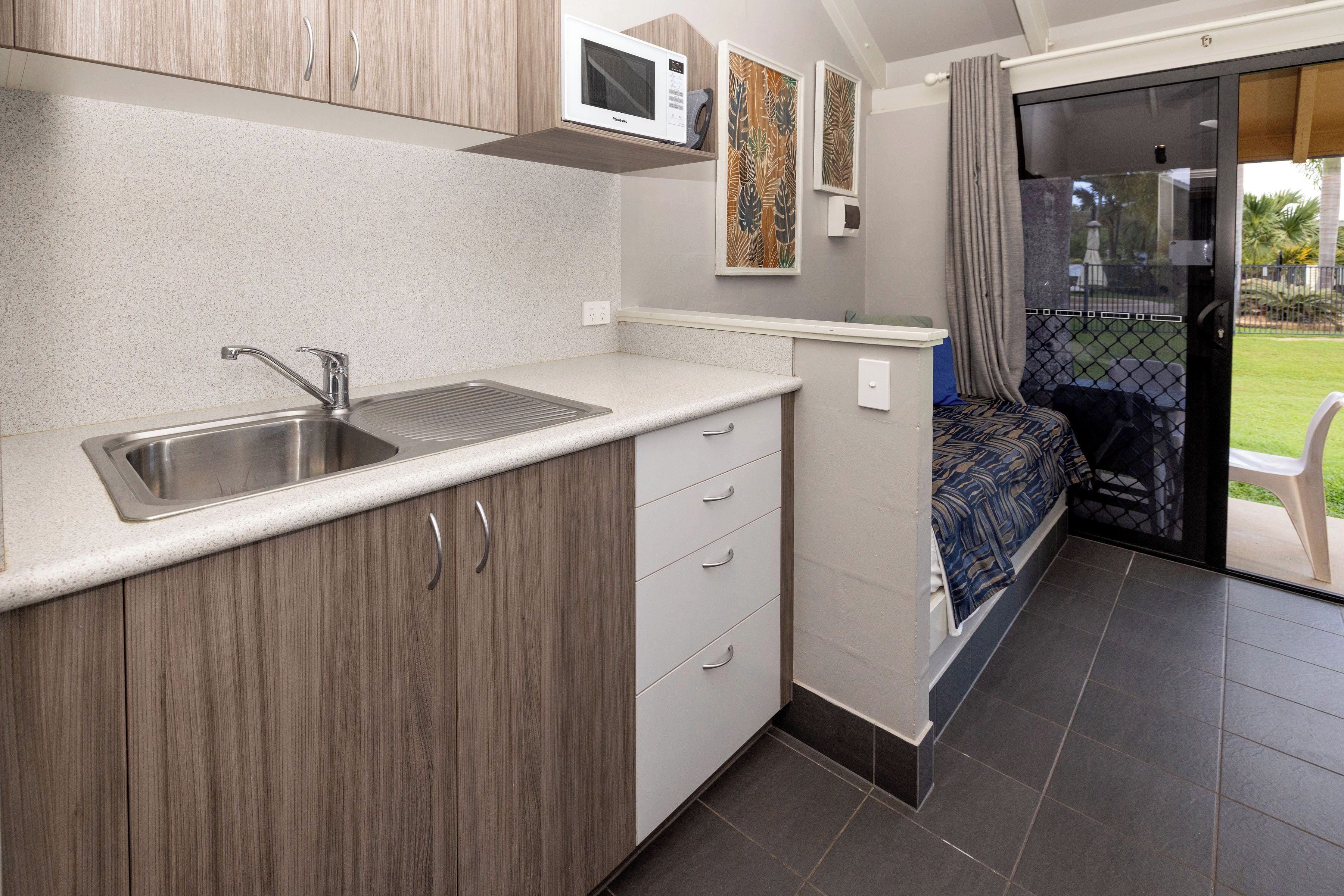 A compact kitchen with a microwave, sink, and wooden cabinets.