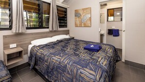 A bedroom with a bed, a nightstand, a window with curtains, a wall art piece, and a bathroom visible through an open door.