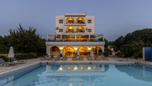 Ein mehrstöckiges Hotel mit Schwimmbad, Sitzgelegenheiten im Freien und Balkonen mit Pflanzen.