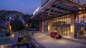 A modern hotel with a covered entrance, a swimming pool, and a red car parked in front. - Hyatt Centric Hebbal Bengaluru (Bengaluru)