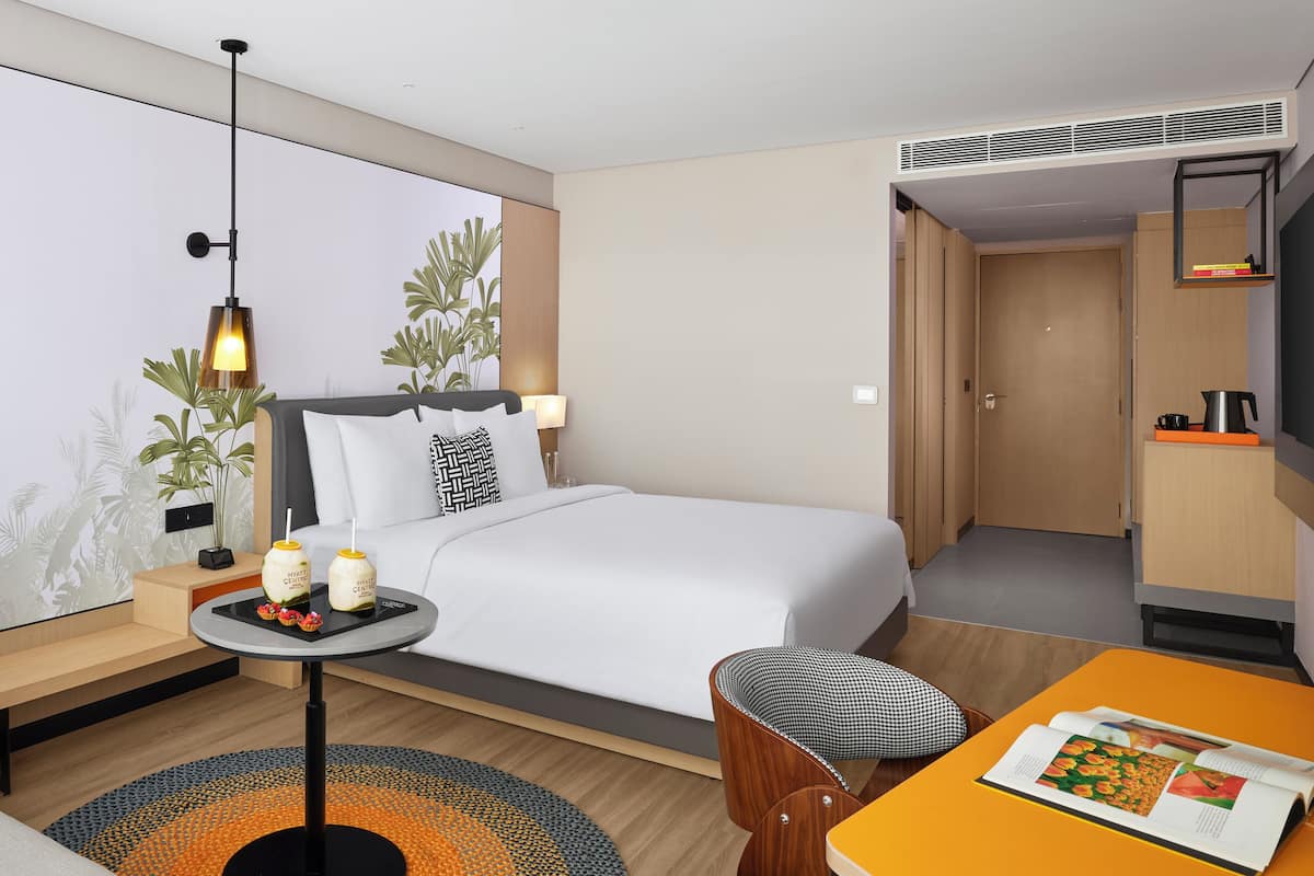 Une chambre d’hôtel avec un lit, une table de chevet, une lampe et une petite table sur laquelle se trouve un magazine.