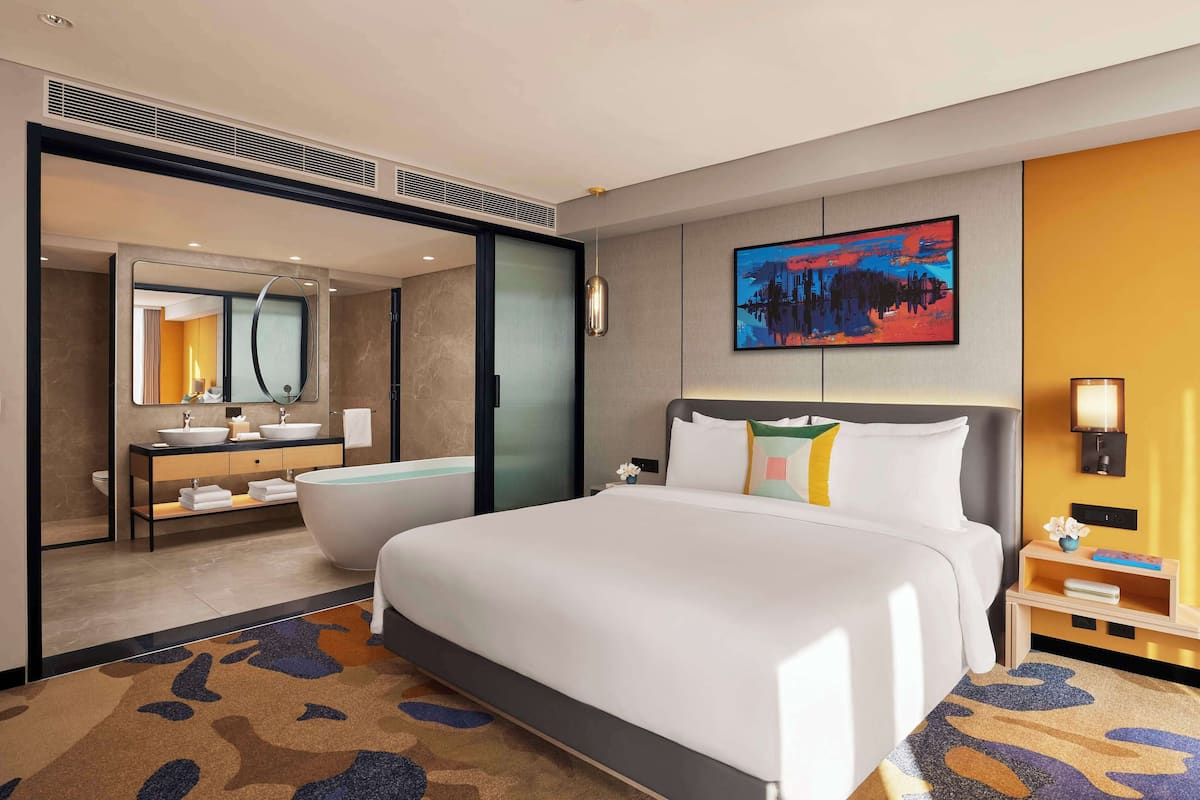 Une chambre d’hôtel avec un grand lit, une salle de bain avec une baignoire, un grand miroir et un tableau au mur.