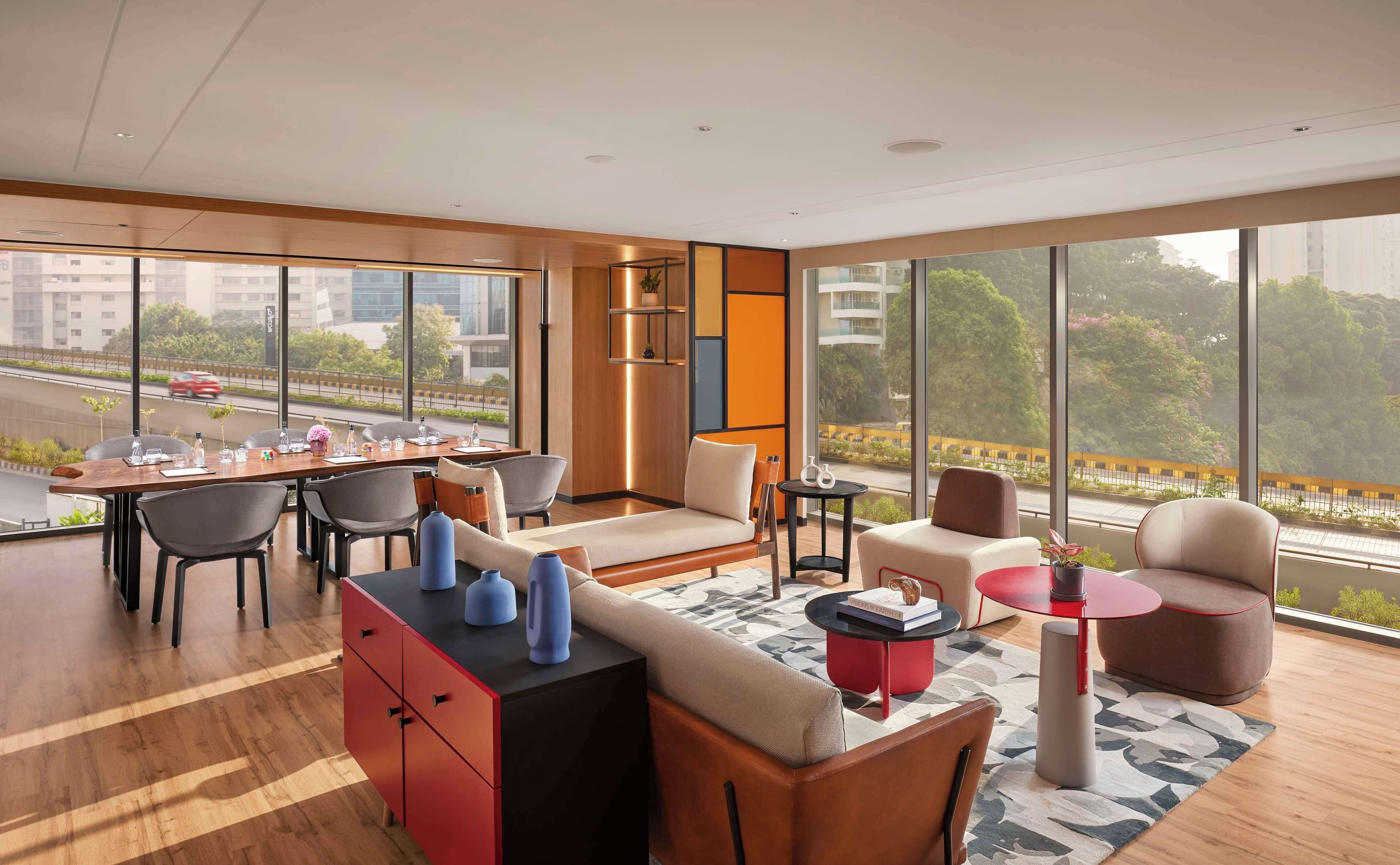 A modern hotel room with a dining area, a sofa, and a view of the city.