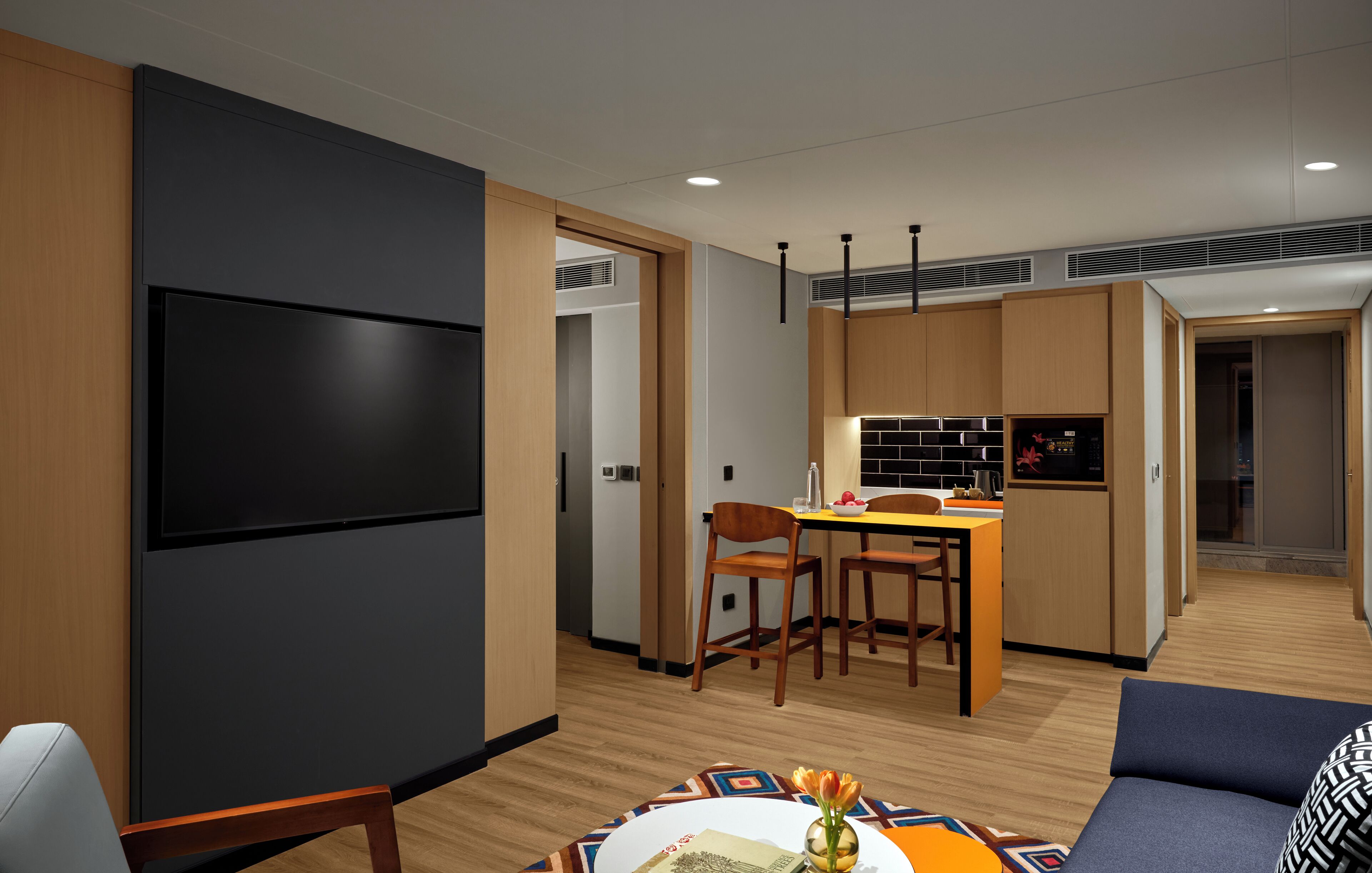 Una habitación de hotel moderna con televisor de pantalla plana, muebles de madera, un área de comedor y una kitchenette.