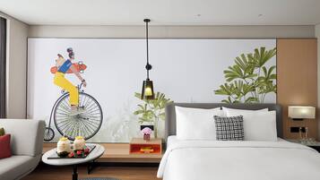 Habitación de hotel moderna con una cama grande, un sofá, una mesita con adornos, un mural en la pared y una planta en maceta.