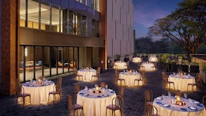 An outdoor dining area with multiple round tables set for guests, surrounded by a modern building with large windows and a brick facade. - Hyatt Centric Hebbal Bengaluru (Bengaluru)