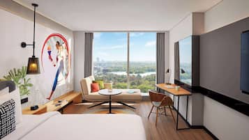 Una habitación de hotel moderna con una cama grande, un escritorio con silla, un sofá, un televisor y un ventanal con vistas a la ciudad.