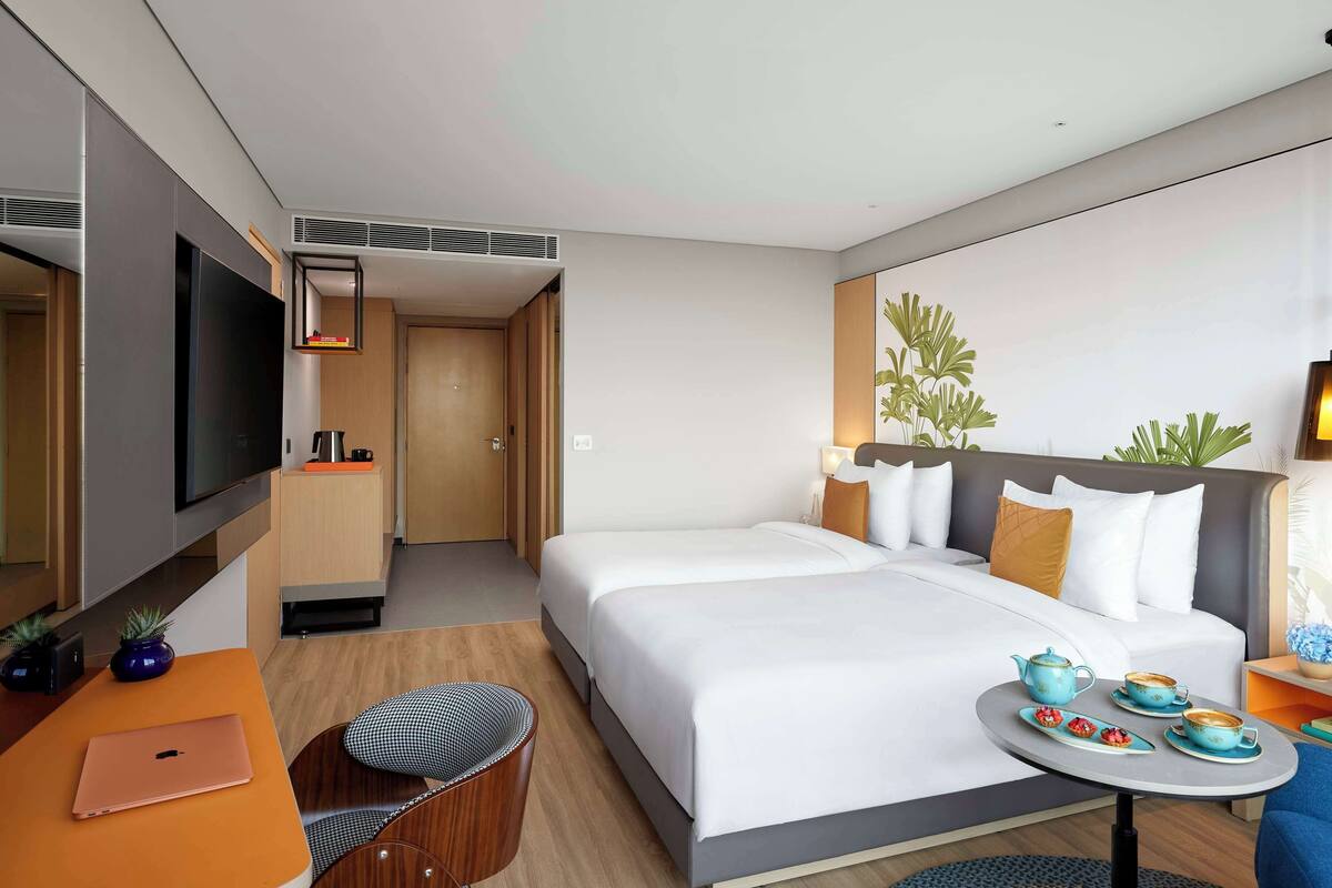 Une chambre d’hôtel moderne avec un grand lit, un bureau avec un ordinateur portable, une petite table avec des théières et un téléviseur fixé au mur.