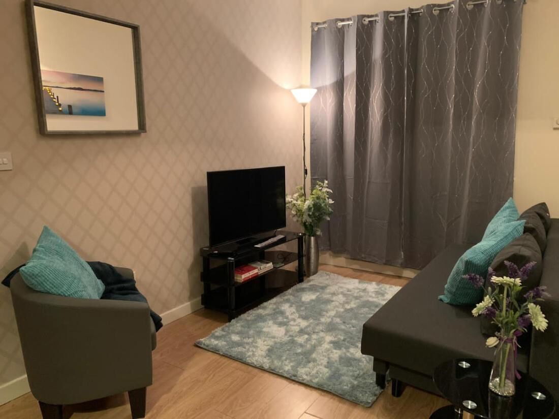 A living room with a flat-screen TV, a sofa, a chair, a rug, a lamp, and a curtain.