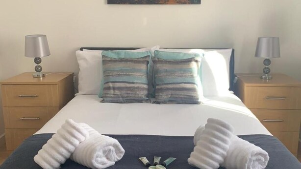 Cama bem arrumada com duas toalhas, um quadro de um elefante e uma mesa de cabeceira com abajur.