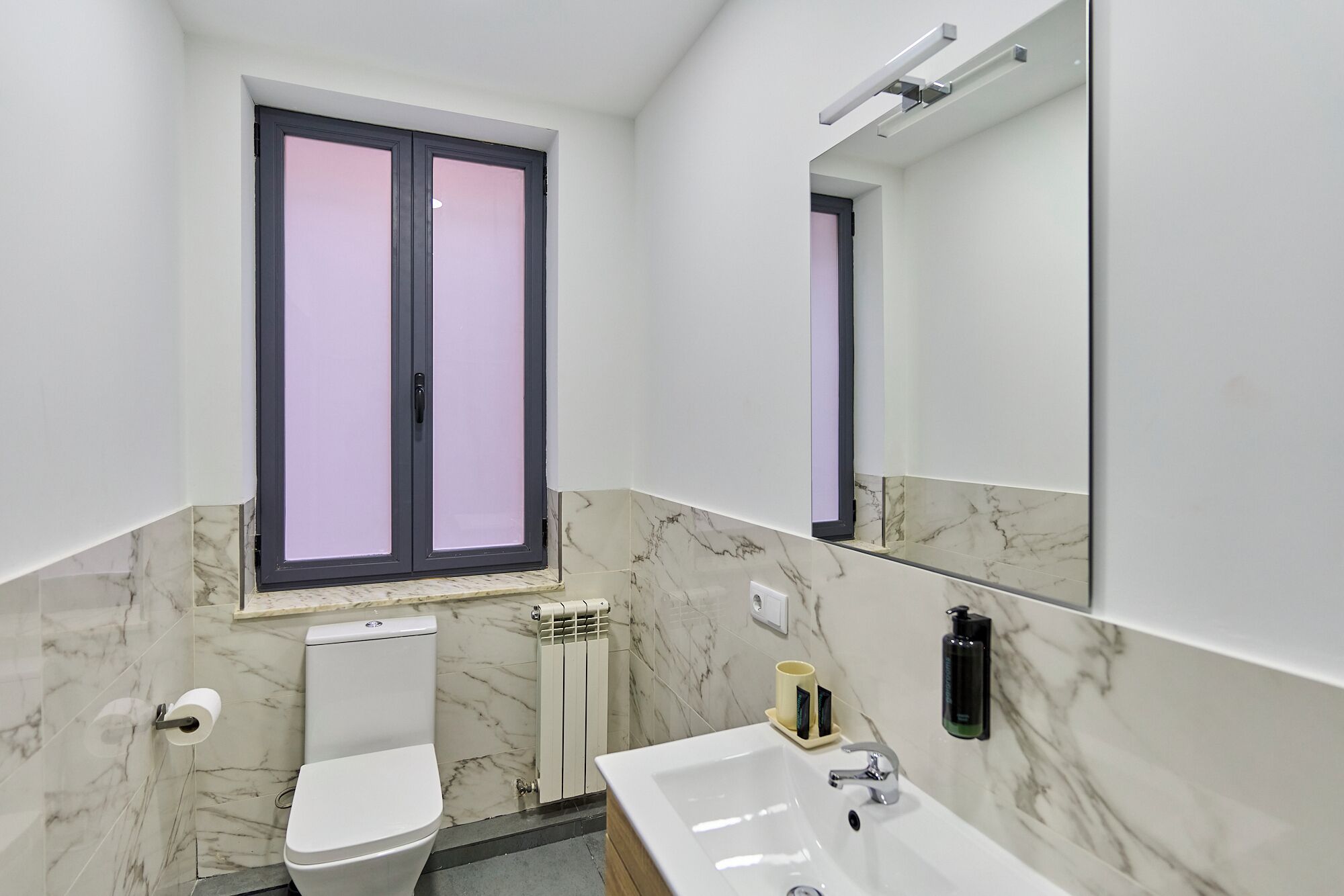 A modern bathroom with a toilet, sink, and a window with frosted glass.