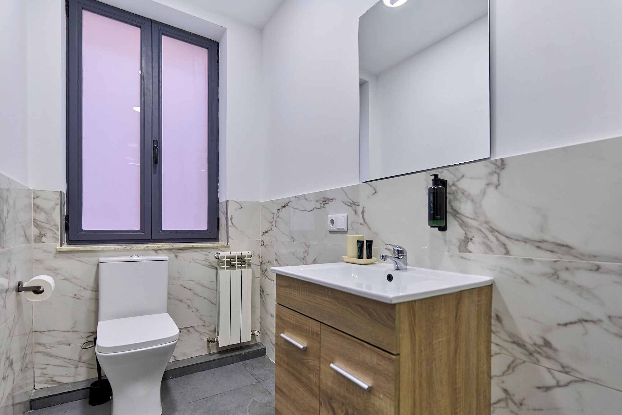A modern bathroom with a toilet, vanity, and a large mirror.