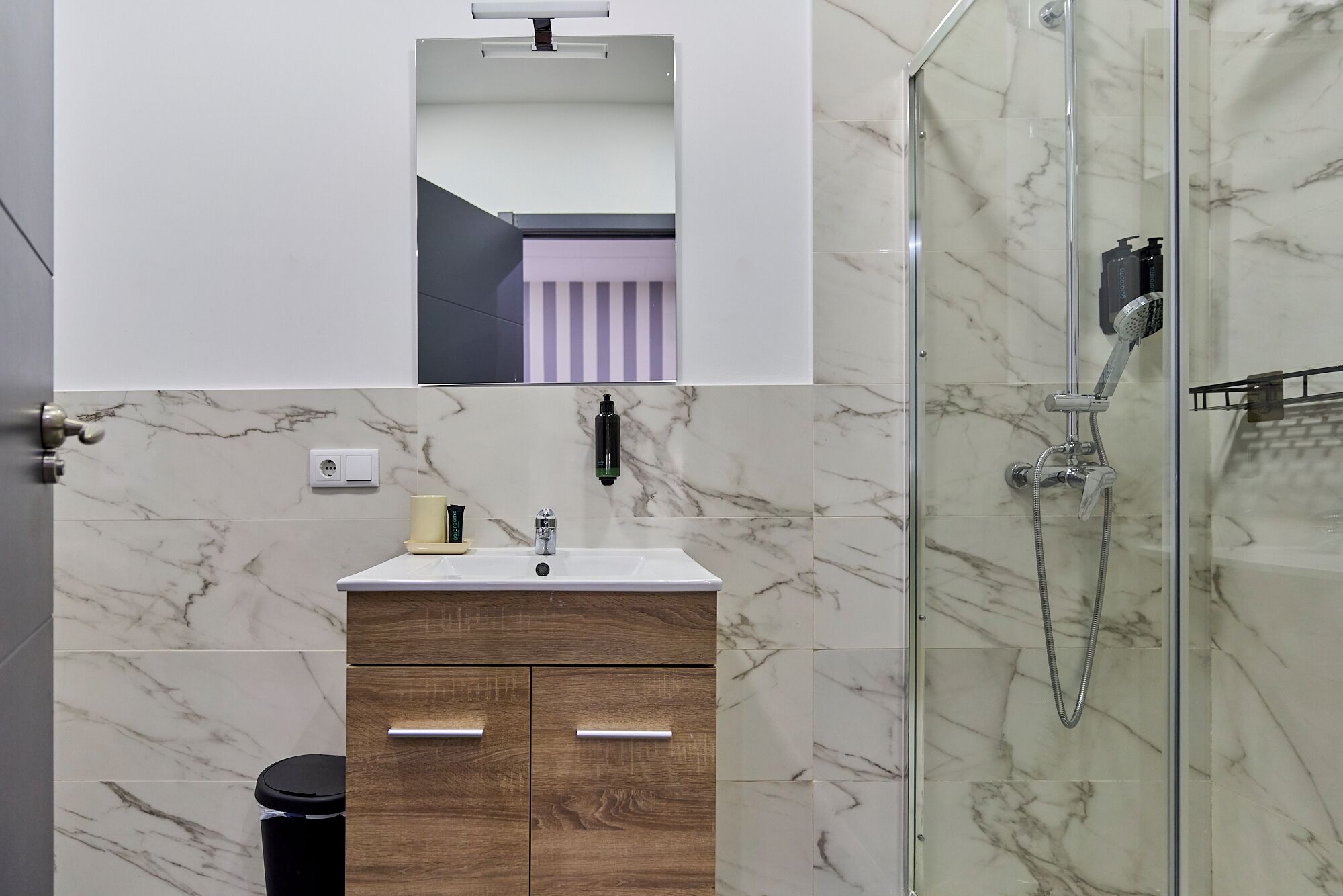 A modern bathroom with a marble shower, a vanity with a mirror, and a toilet.