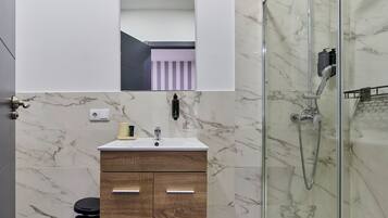 A modern bathroom with a marble shower, a vanity with a mirror, and a toilet.