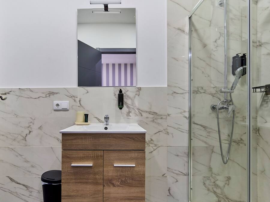 A modern bathroom with a marble shower, a vanity with a mirror, and a toilet.