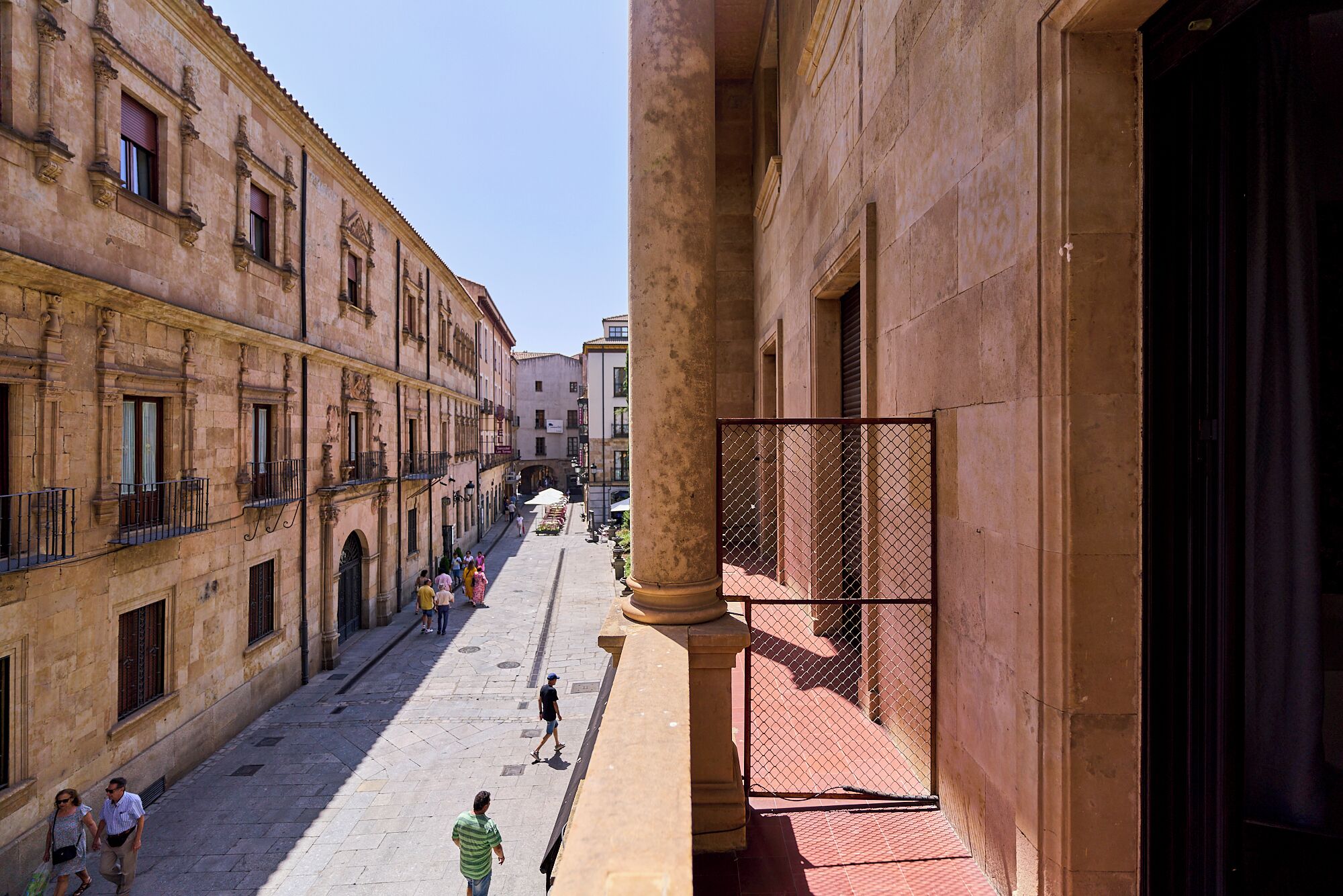 A narrow street with buildings on both sides, featuring balconies and a pedestrian walkway.