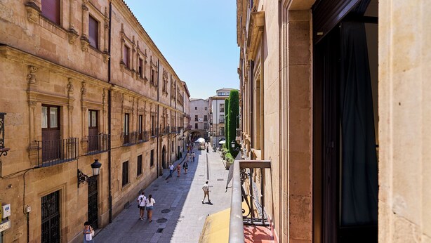 A narrow street with historic buildings, a clear sky, and pedestrians. - Apartamentos Margarita by gaiarooms  (Salamanca)
