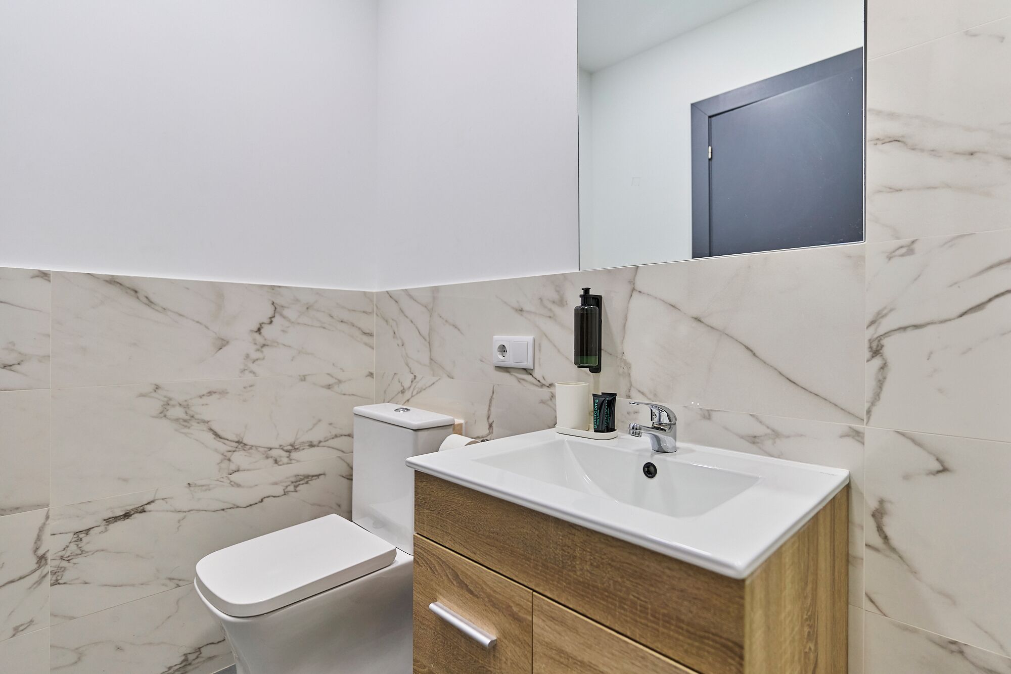 A bathroom with a toilet, sink, and mirror.