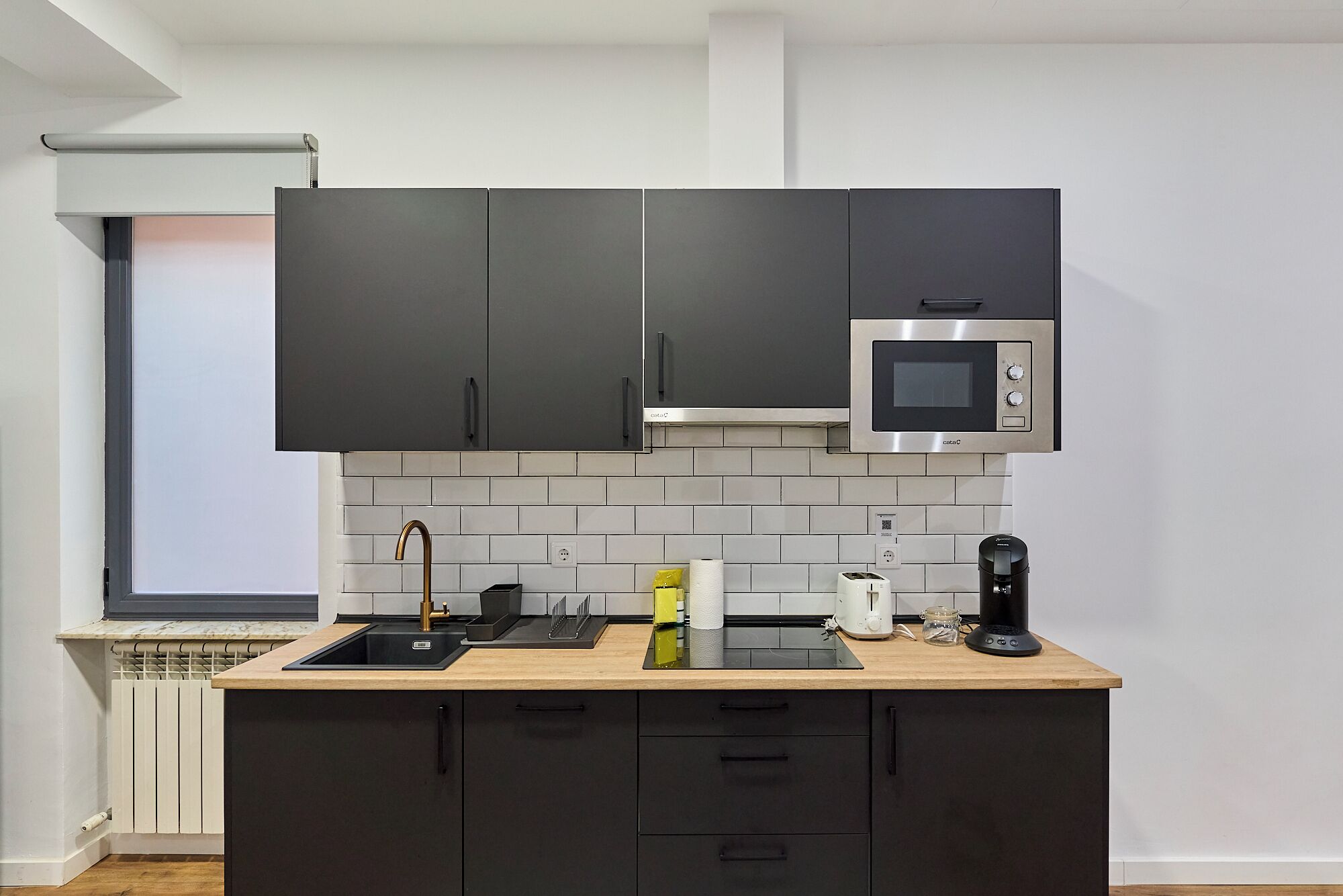 Una cocina compacta con armarios oscuros, un microondas, un lavamanos y una cafetera.