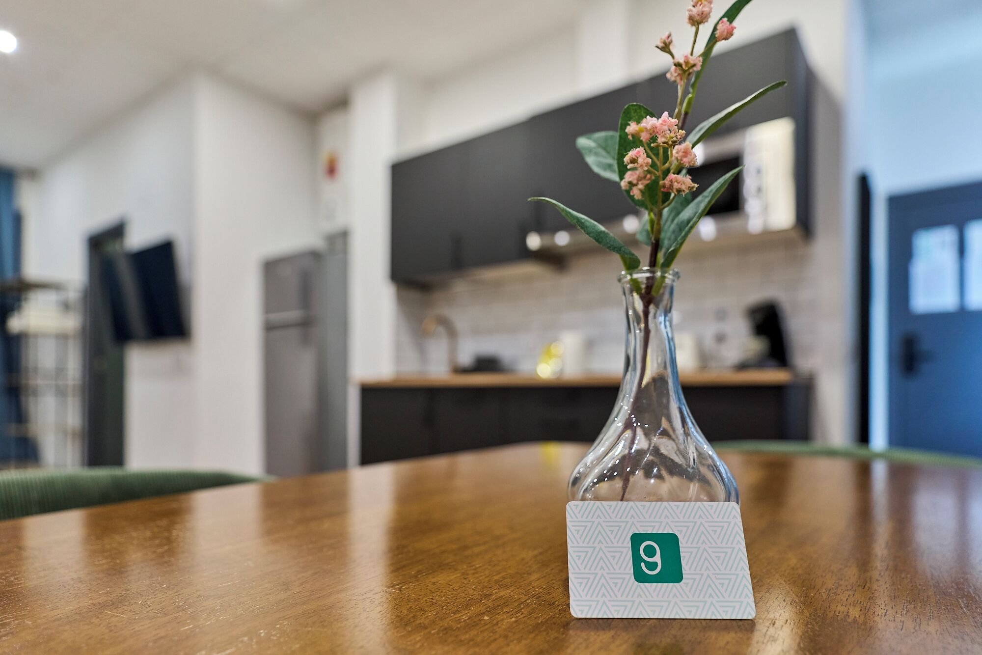 Et træbord med en klar glasvase med lyserøde blomster og et kort med tallet 9.