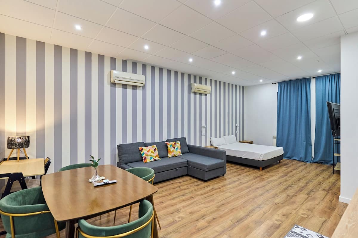 Une chambre d’hôtel avec un canapé gris, une table à manger en bois, un lit et un téléviseur.