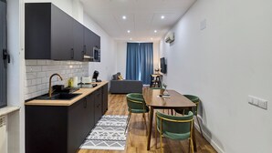 A compact kitchen with a microwave, sink, and dark cabinets. A dining area with a wooden table and green chairs is visible. - Apartamentos Margarita by gaiarooms  (Salamanca)