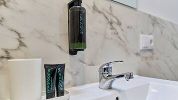 A bathroom with a marble wall, a white sink, a chrome faucet, and two tubes of body lotion labeled 'gairoom'.