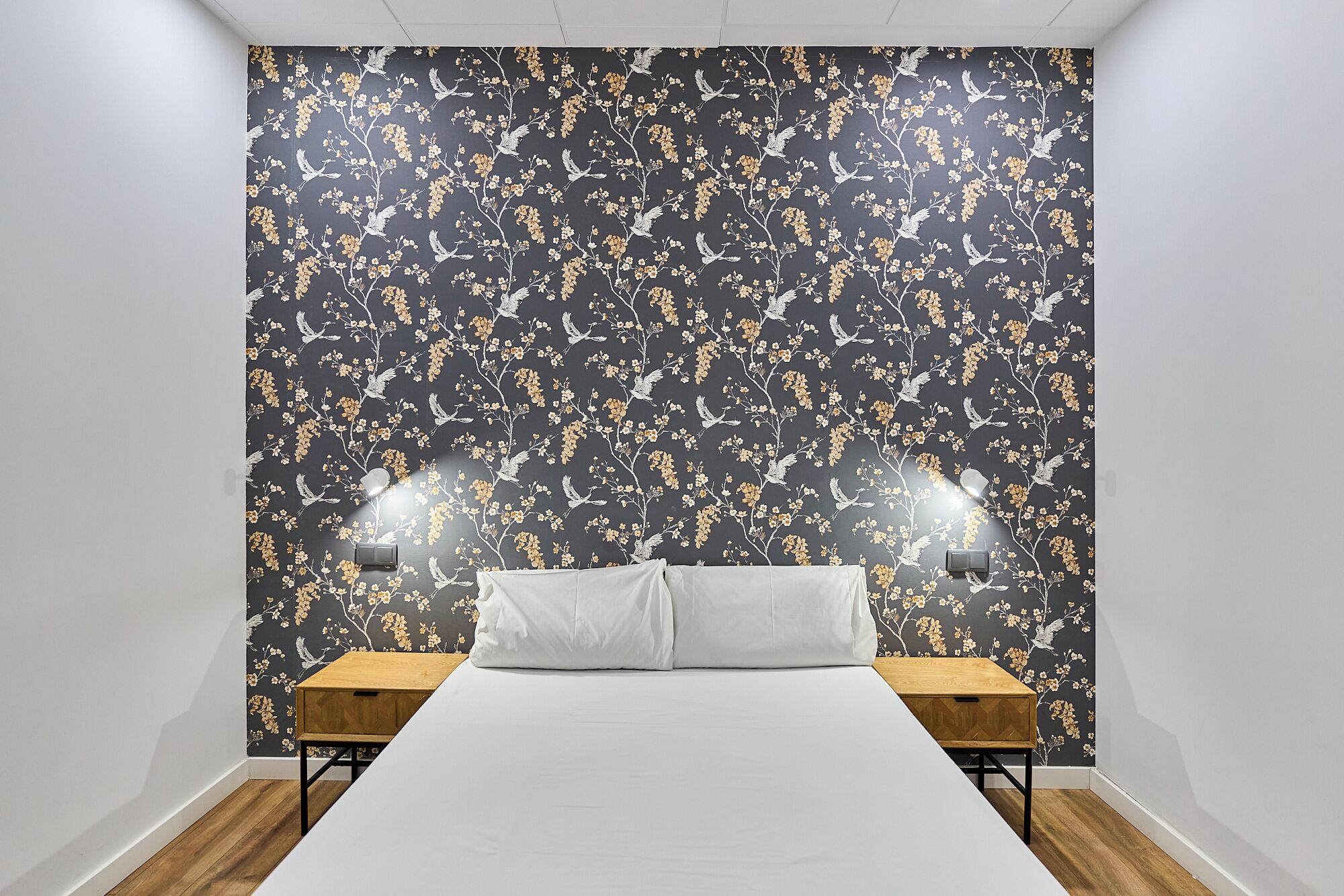 A bedroom with a large bed, two bedside tables, and a wall with a floral wallpaper.