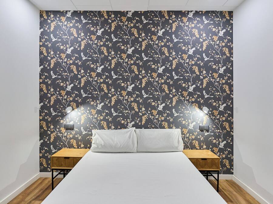 A bedroom with a large bed, two bedside tables, and a wall with a floral wallpaper.