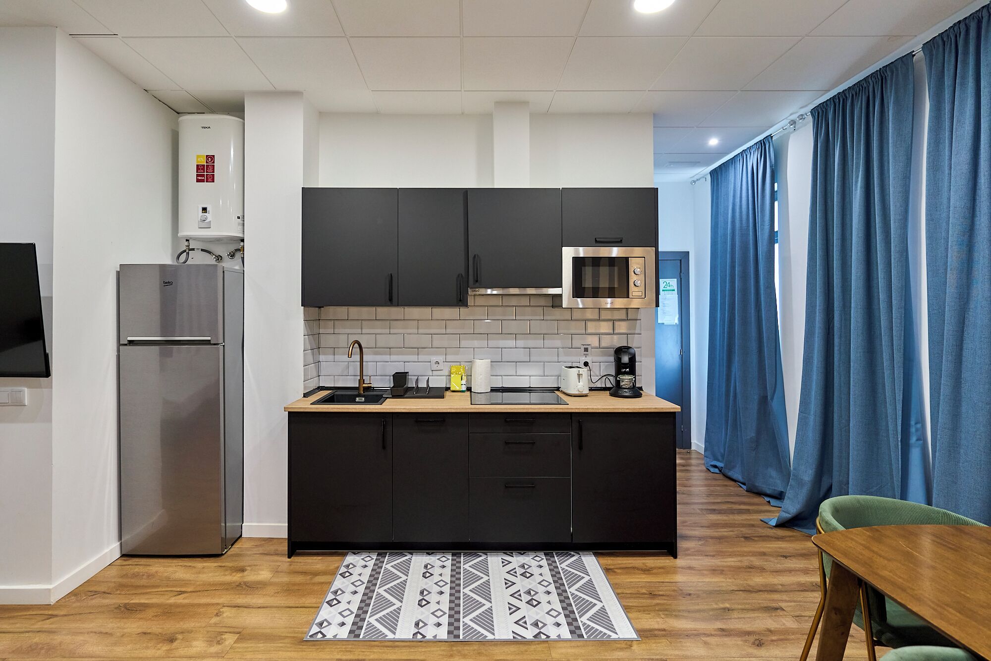 Una cocina moderna con armarios negros, un refrigerador de acero inoxidable, un microondas y un lavamanos.