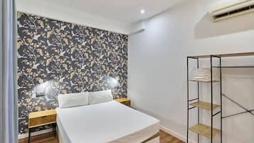 A bedroom with a bed, a nightstand, a wall-mounted shelf, and an air conditioning unit.