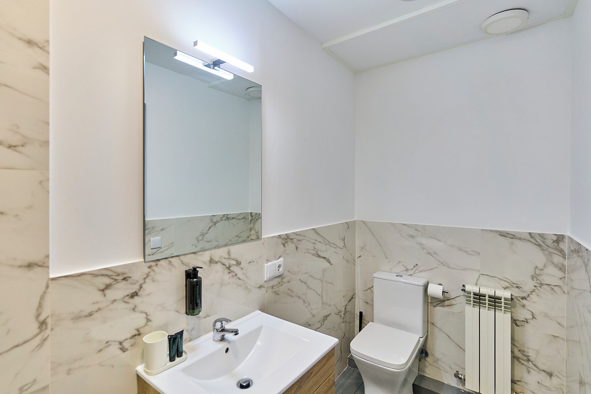 A bathroom with a marble wall, a sink, a toilet, and a mirror.