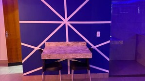 Een kamer met een blauwe wand met een wit geometrisch patroon, een houten tafel met twee zwarte stoelen en een rode bank.