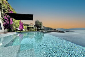 An infinity pool with clear water, surrounded by lush greenery and a view of distant mountains. - In Costa Relais & Luxury Suites (Vietri sul Mare)