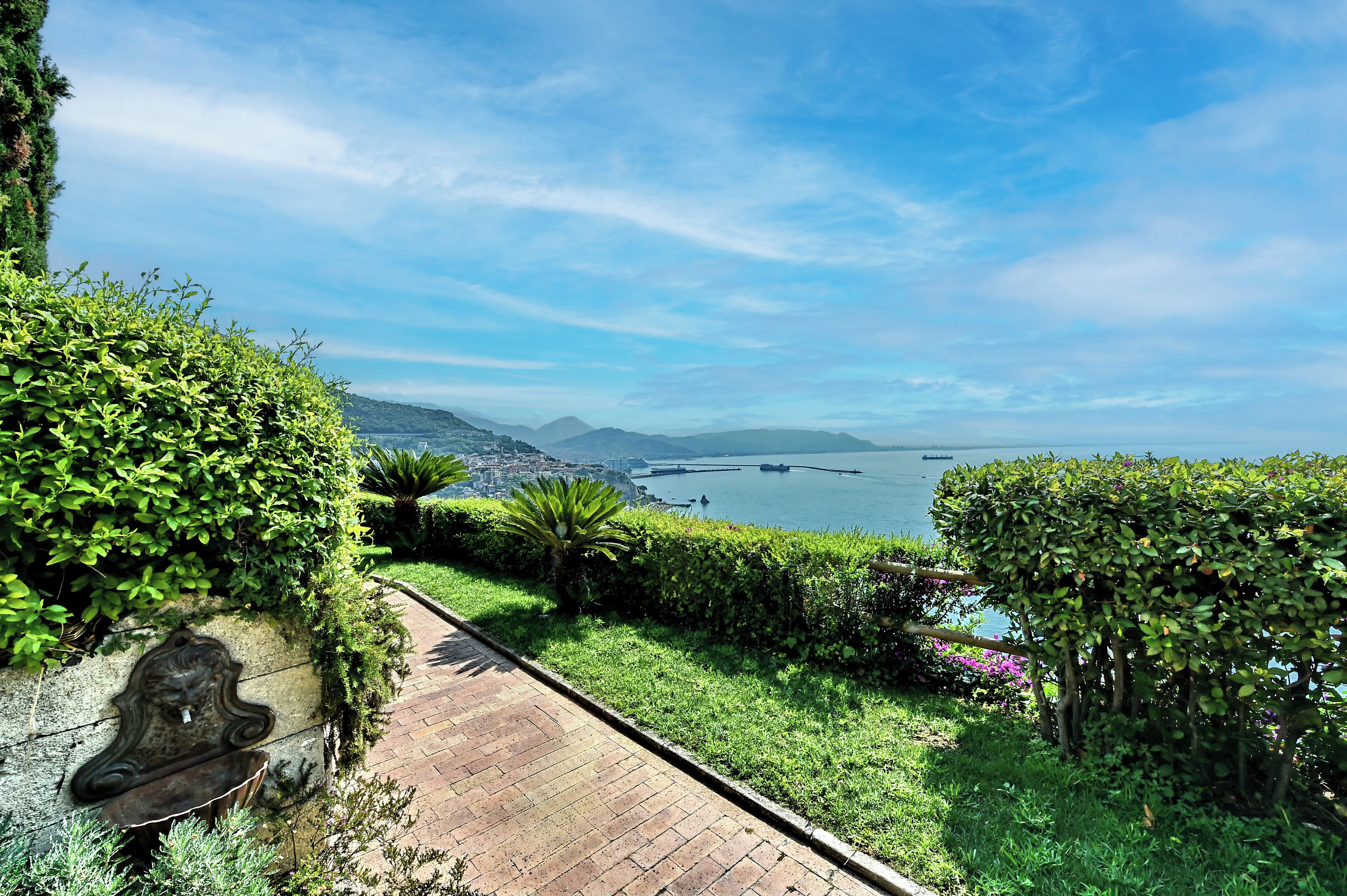 A paved pathway with a view of a body of water and distant mountains.