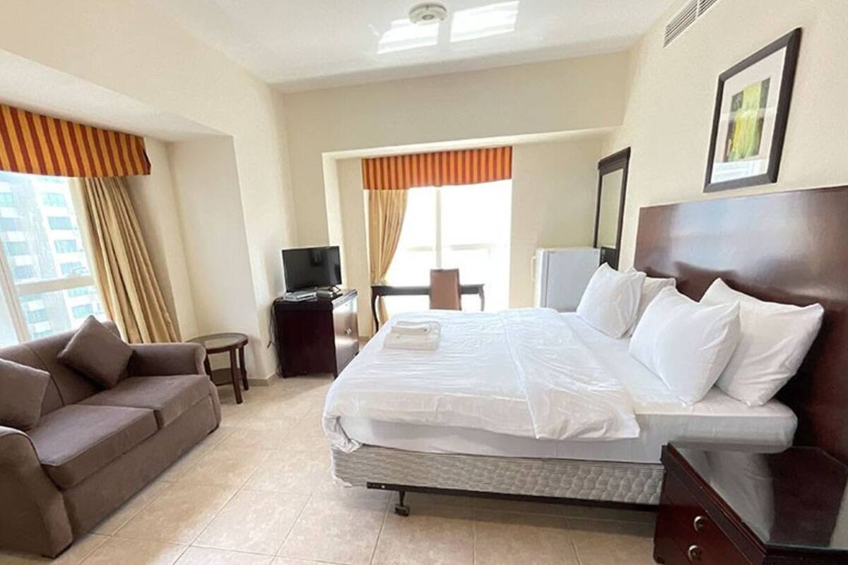 A hotel room with a bed, a sofa, a TV, and a desk.