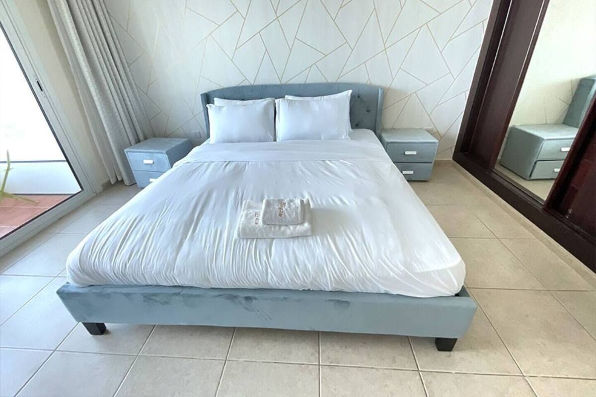 A modern bedroom with a large bed, two bedside tables, a nightstand, and a view of the outdoors.