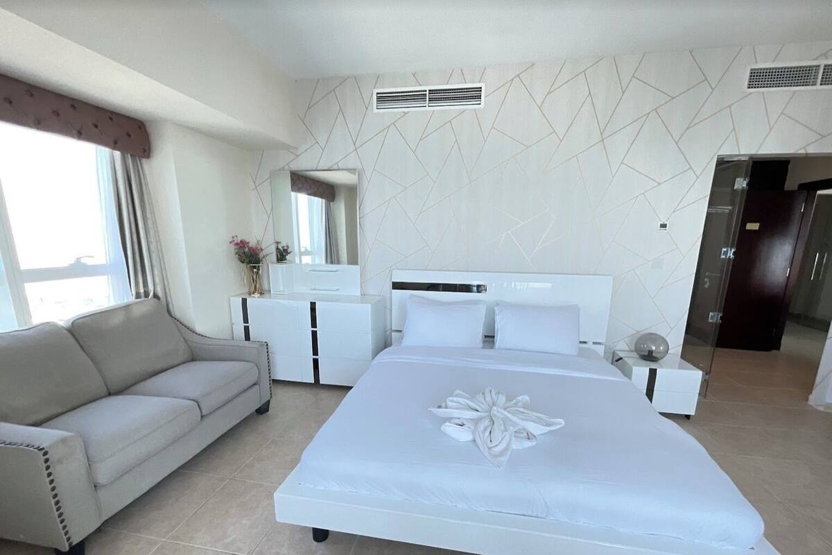A modern hotel room with a large bed, a sofa, a dresser, and a mirror.